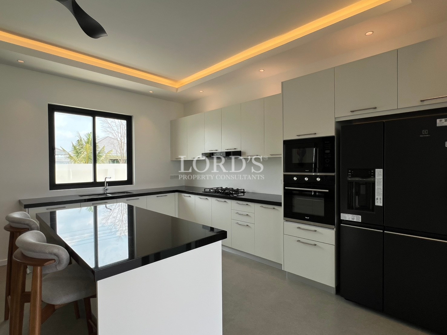 Modern white kitchen with black countertops, island, built-in oven, and large black refrigerator.