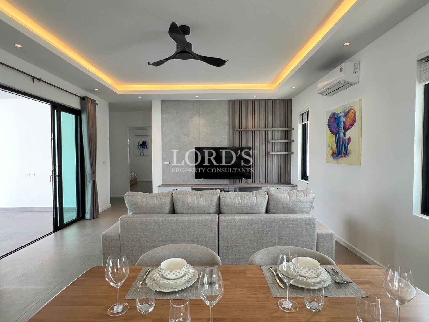 Open-plan living room with dining table, sofa, wall-mounted TV, and LED ceiling lighting.