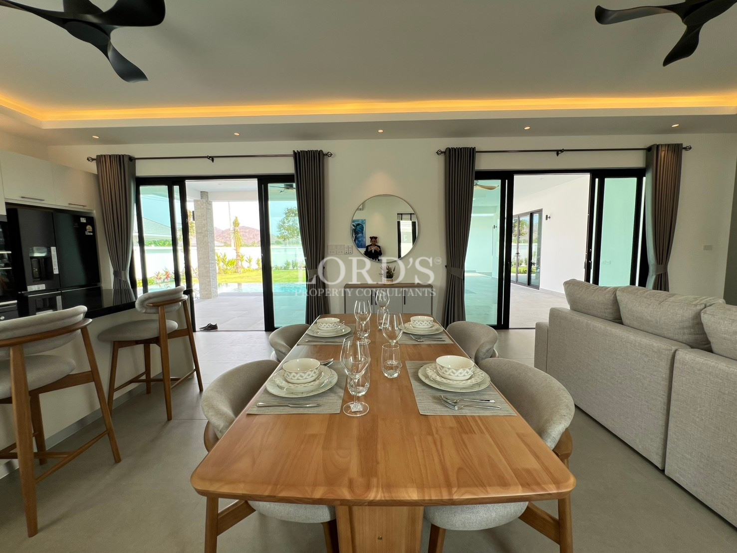 Modern dining area with wooden table set for six, open-plan living space, and large sliding glass doors.
