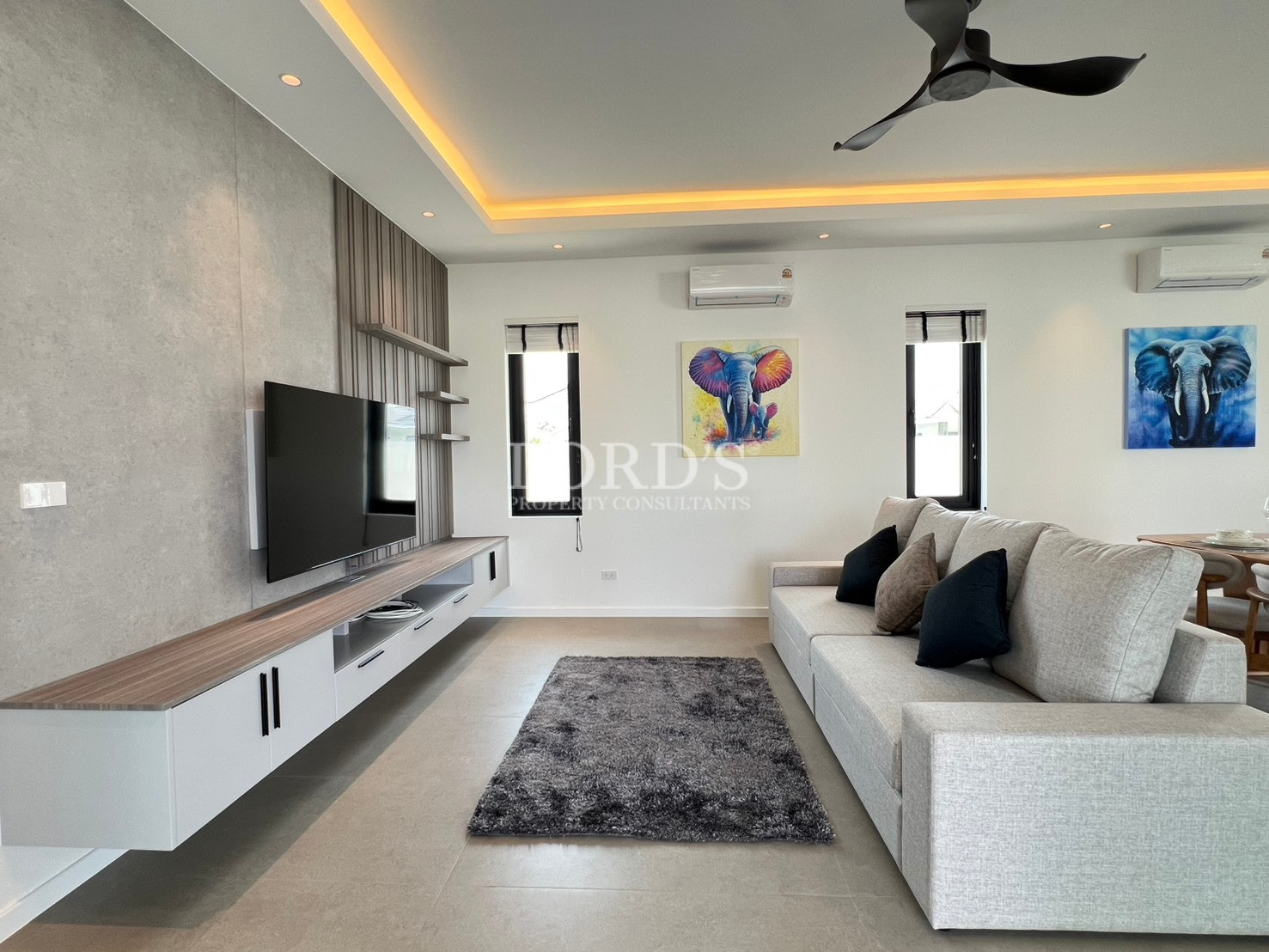Modern living room with wall-mounted TV, floating media unit, and beige sofa.
