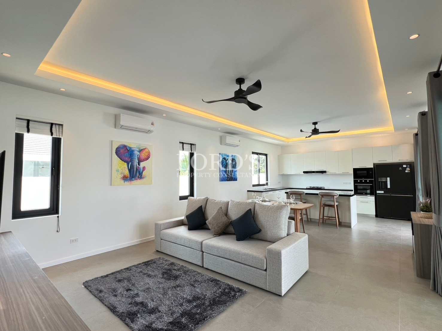 Modern open-plan living room and kitchen with sofa, LED ceiling lighting, and breakfast bar.