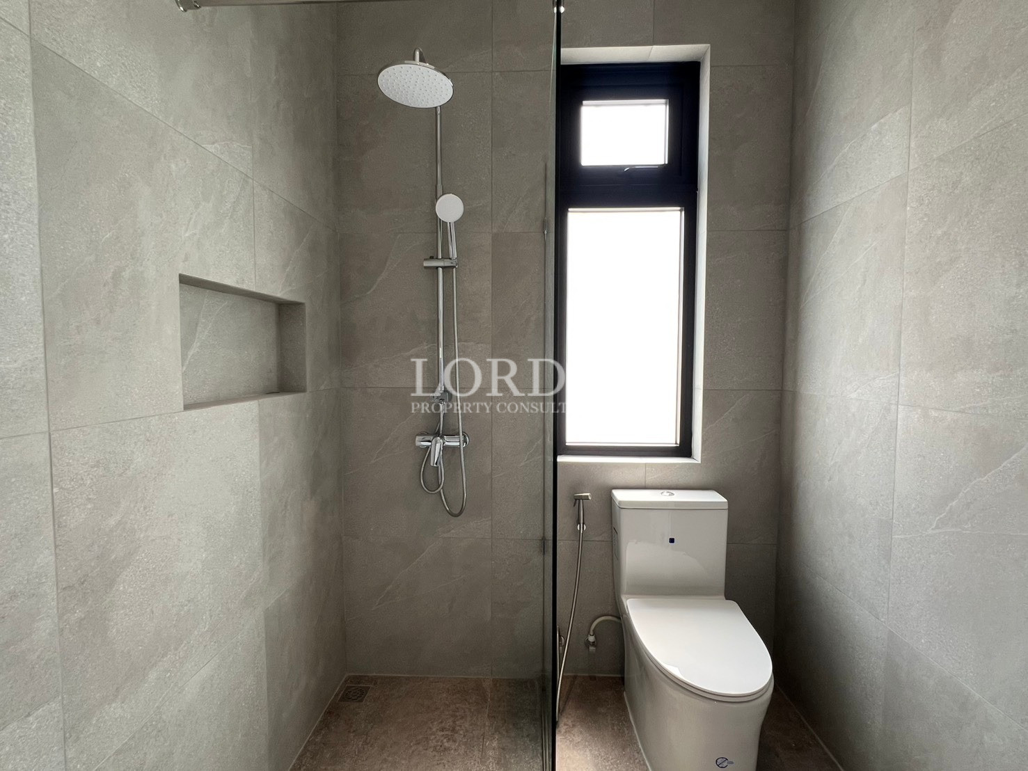 Compact modern bathroom with walk-in shower, rainfall showerhead, and toilet beside tall window.