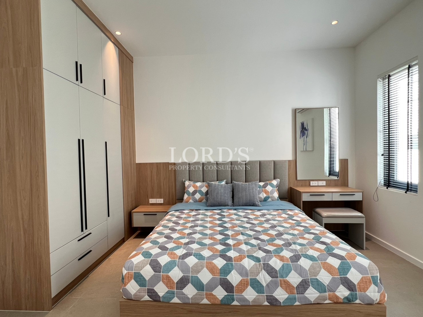 Modern bedroom with built-in wardrobe, geometric patterned bedspread, and wooden vanity desk.