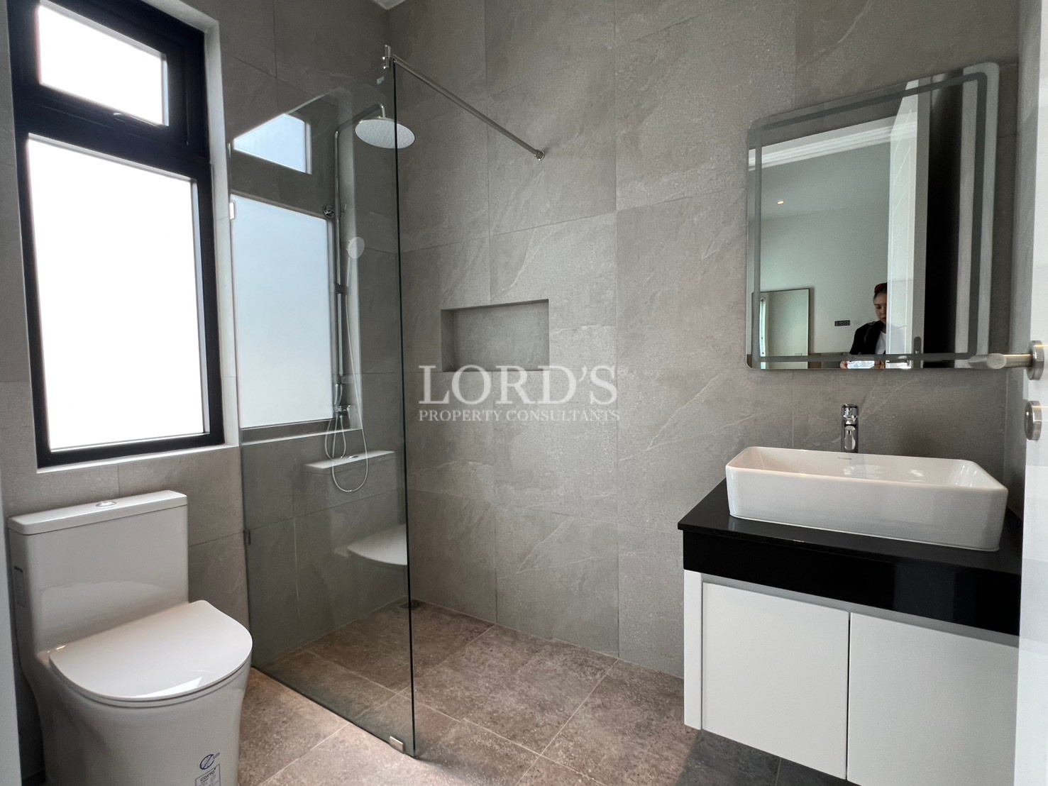 Modern bathroom with glass-enclosed shower, white vessel sink, and gray tiled walls.