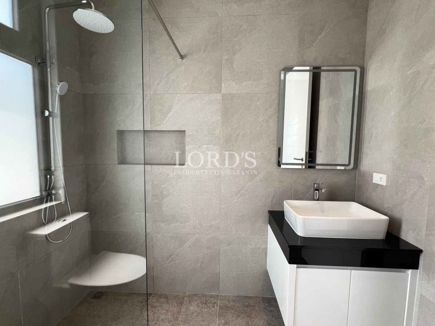 Modern bathroom with glass-enclosed shower, white vessel sink, and gray tiled walls.
