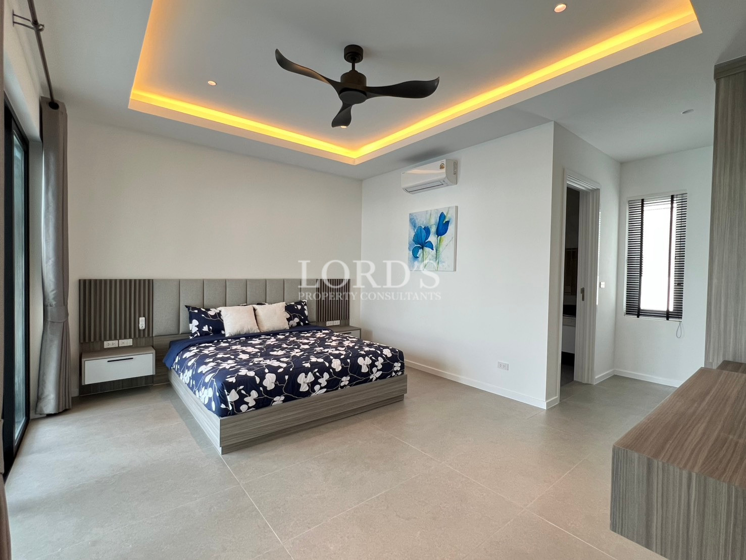 Spacious modern bedroom with king-size bed, LED ceiling lighting, ceiling fan, and en-suite entrance.