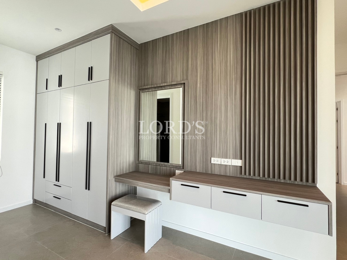 Modern bedroom dressing area with built-in wardrobe, wooden vanity desk, and wall mirror.