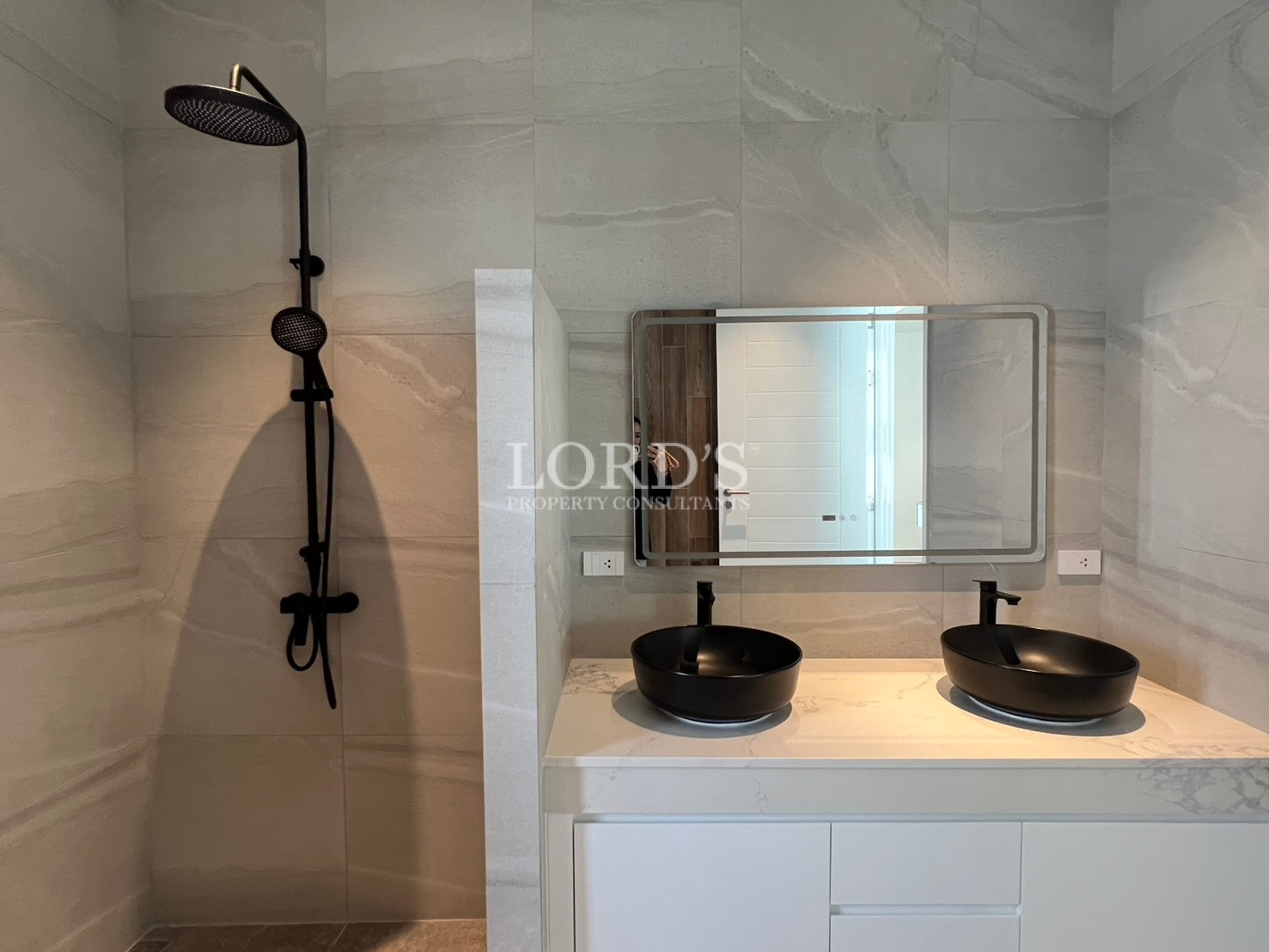 Modern bathroom with double black vessel sinks, wall-mounted mirror, and matte black rainfall shower.