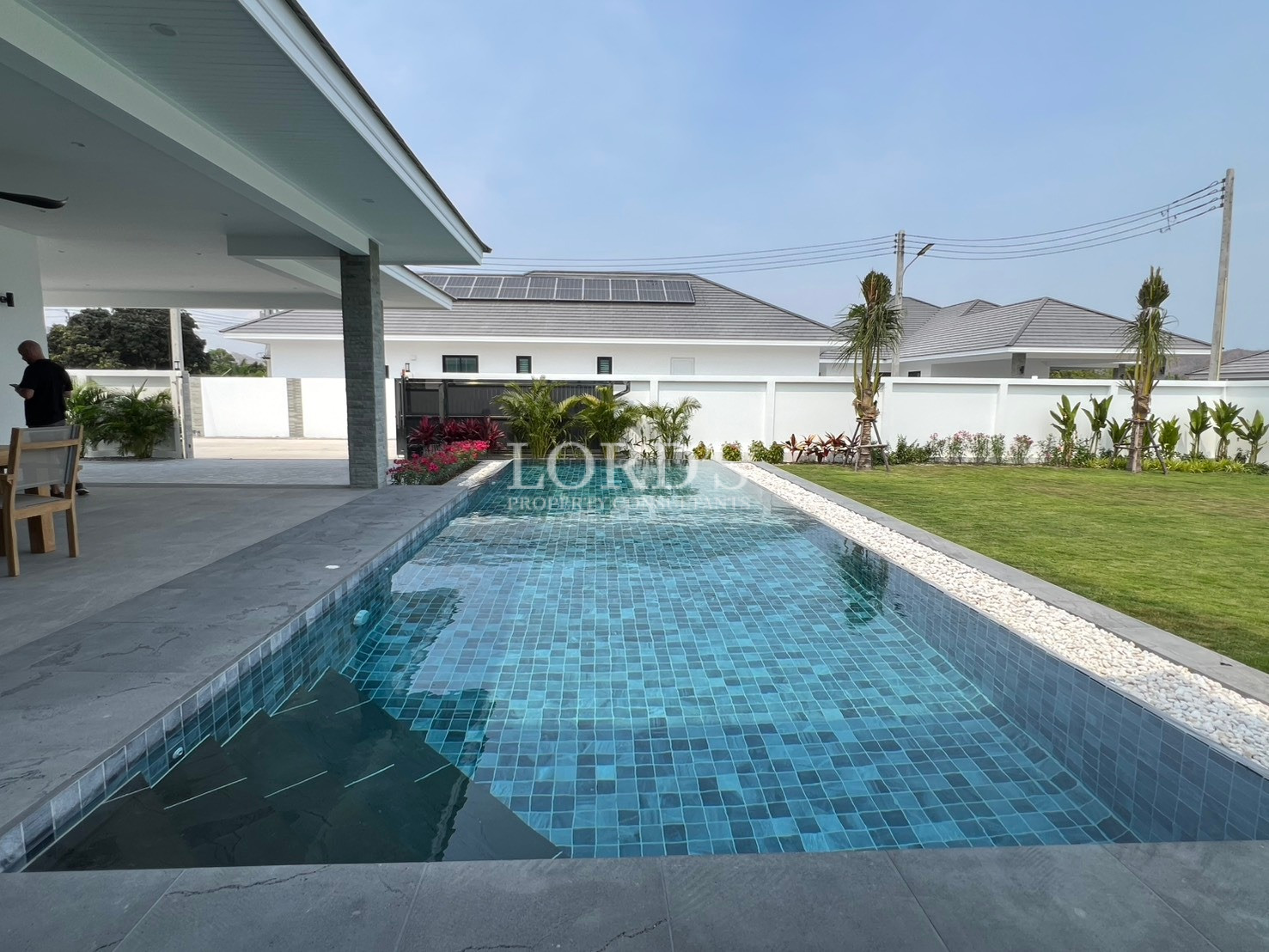 Private rectangular swimming pool with blue mosaic tiles beside a modern villa and landscaped garden.