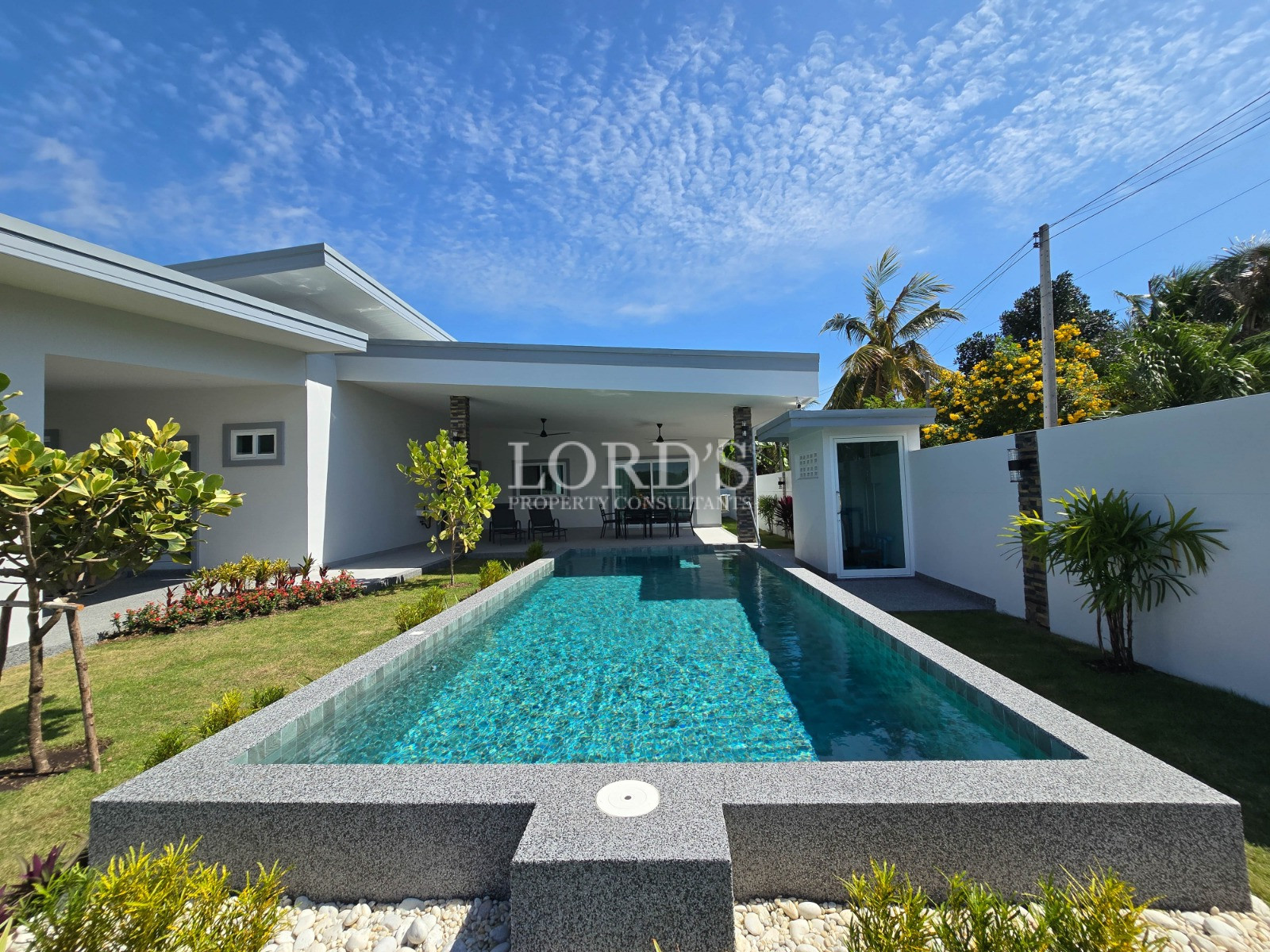 Modern single-story home with rectangular swimming pool, landscaped garden, and covered patio under a blue sky.