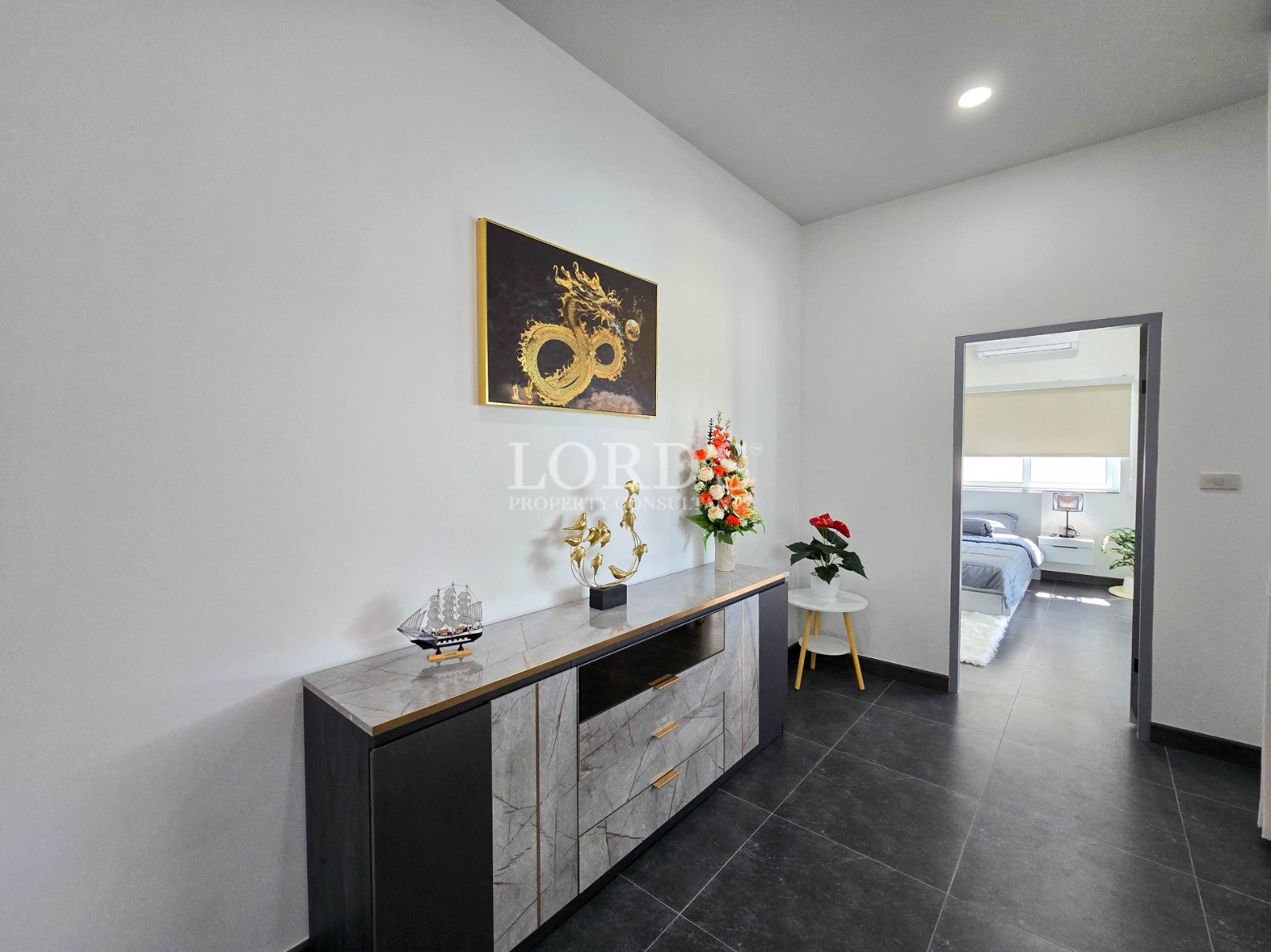 Modern hallway with decorative console table, gold artwork, floral arrangement, and doorway leading to a bedroom.