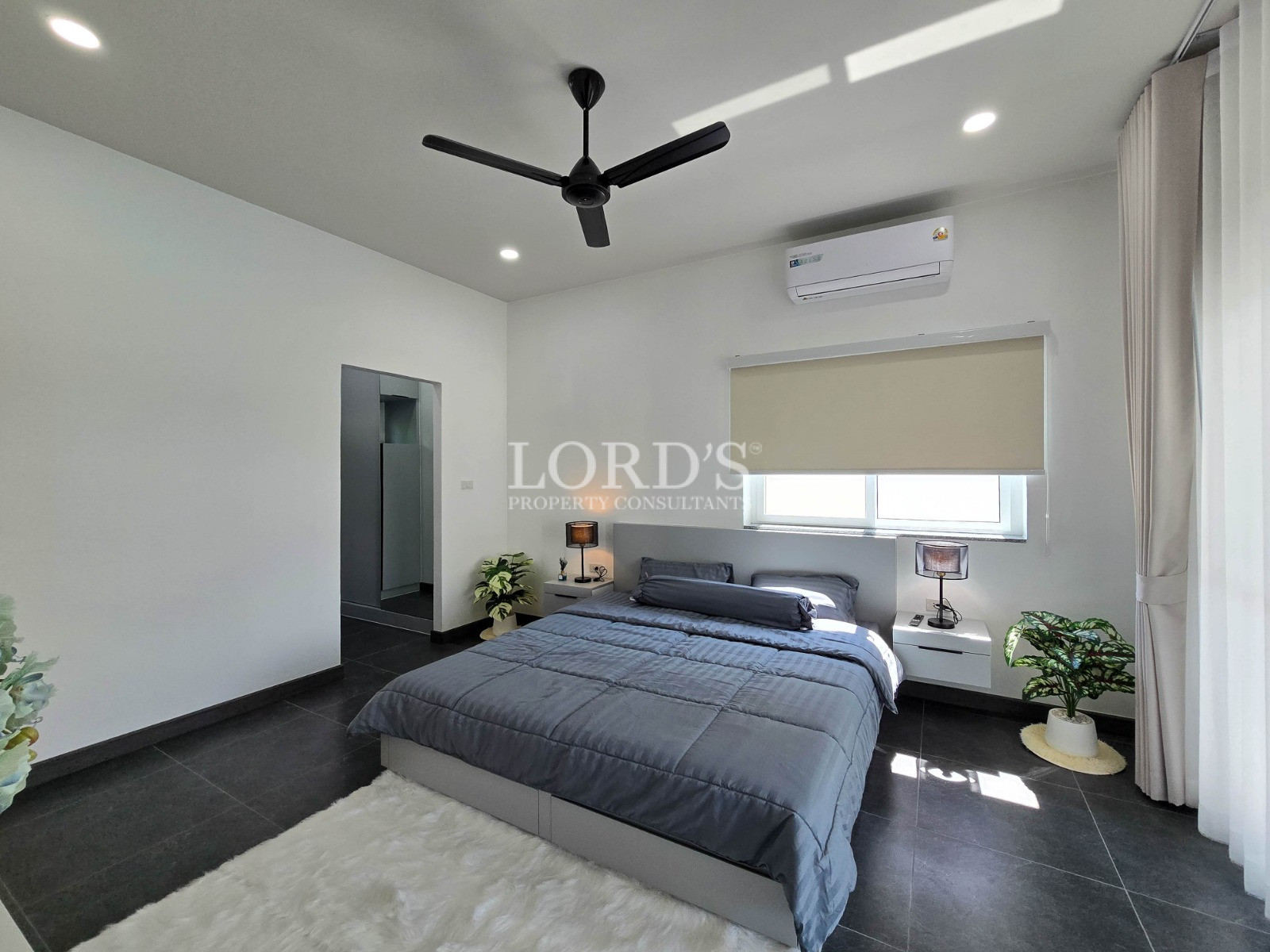 Minimalist bedroom with gray bedding, floating nightstands, ceiling fan, and wall-mounted air conditioner.