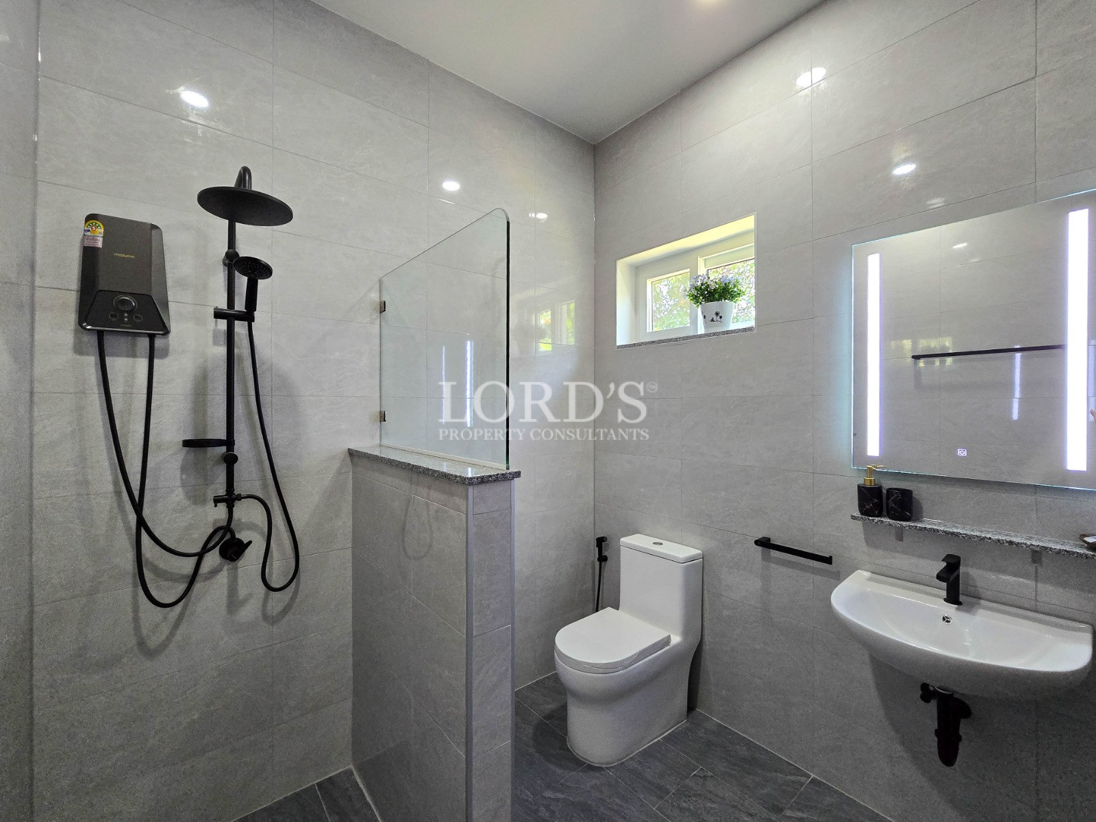 Modern gray-tiled bathroom with walk-in shower, black fixtures, wall-mounted sink, and illuminated mirror.