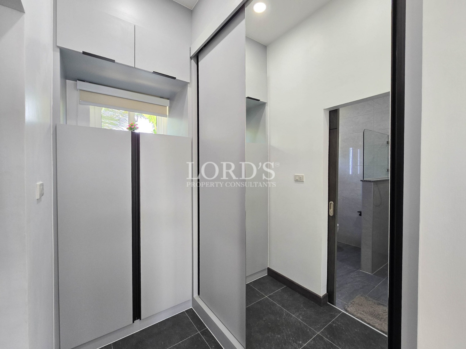 Compact modern entryway with built-in white cabinets, mirrored sliding wardrobe, and dark tiled flooring.