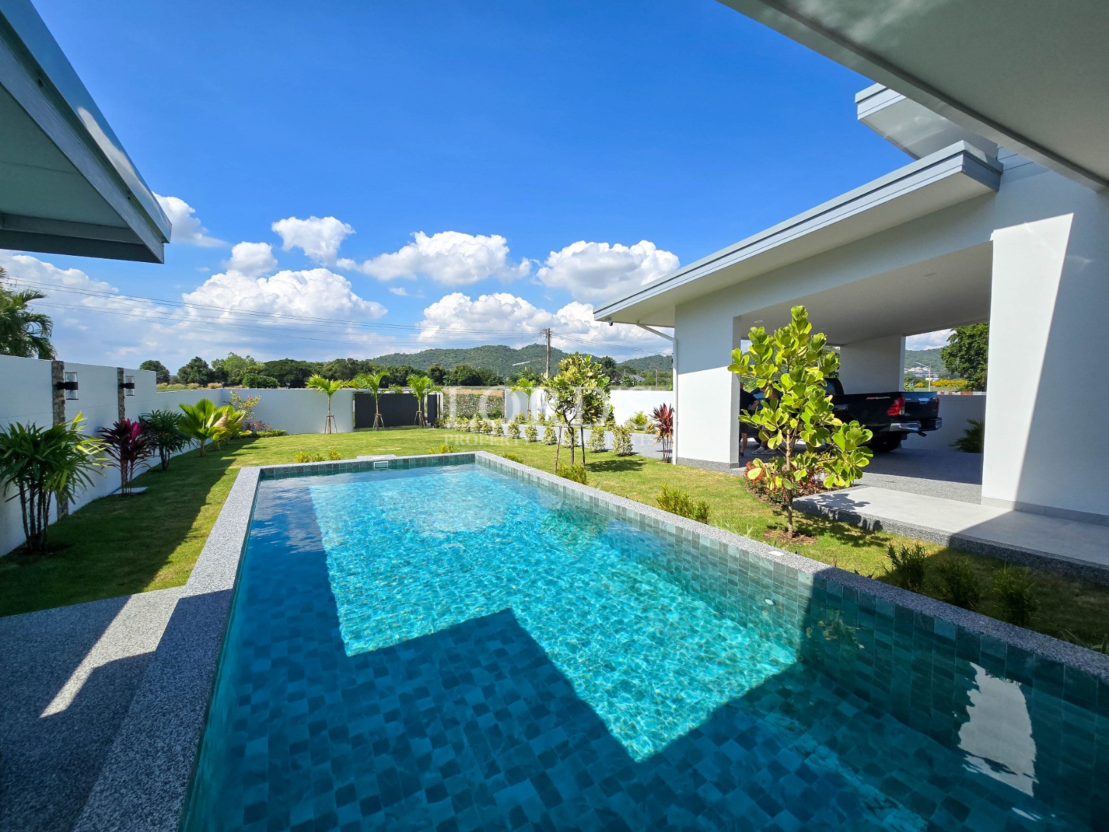 Modern backyard with rectangular swimming pool, landscaped lawn, and covered carport under a bright blue sky.