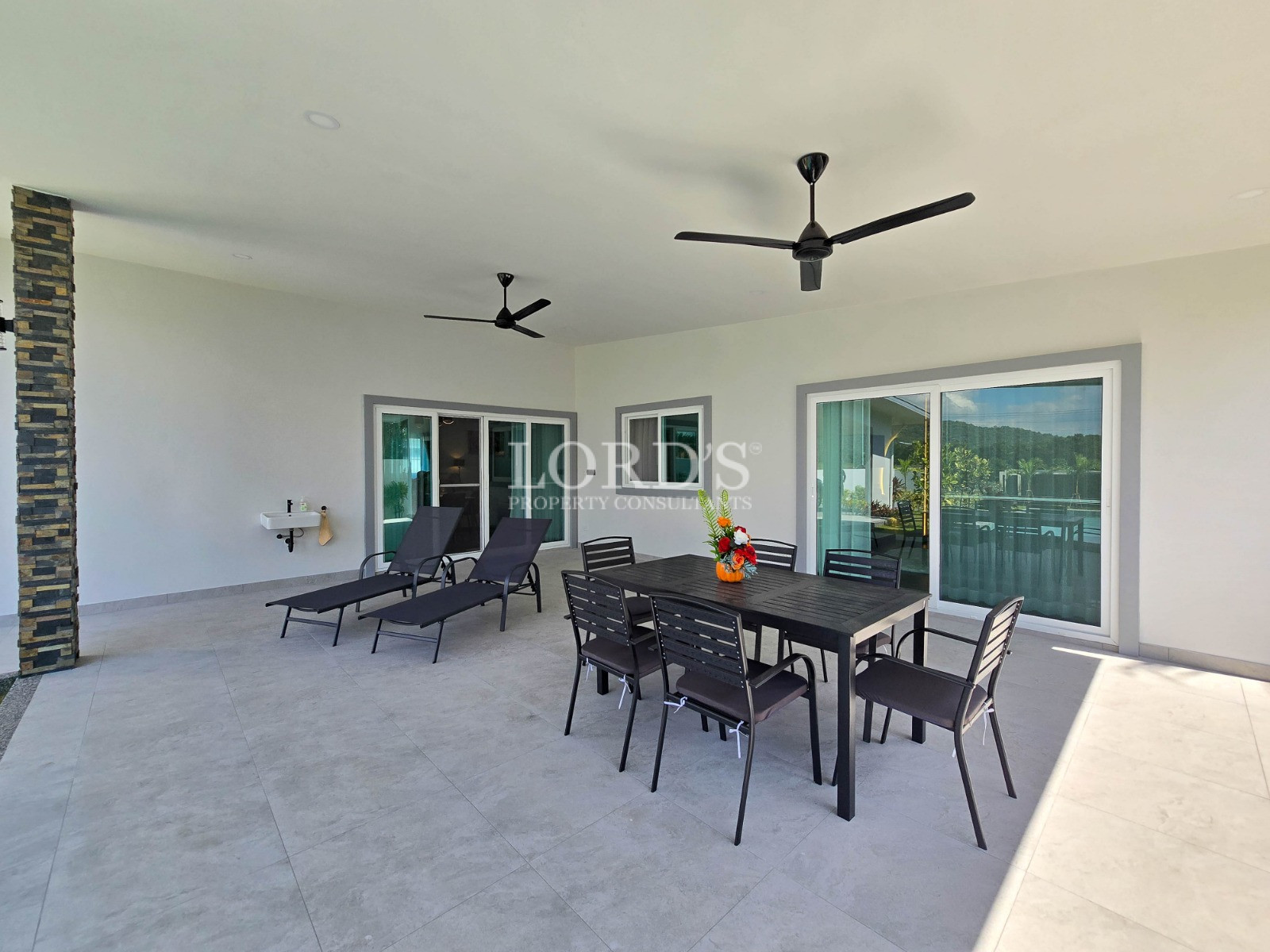 Covered patio with outdoor dining set, lounge chairs, sliding glass doors, and ceiling fans.