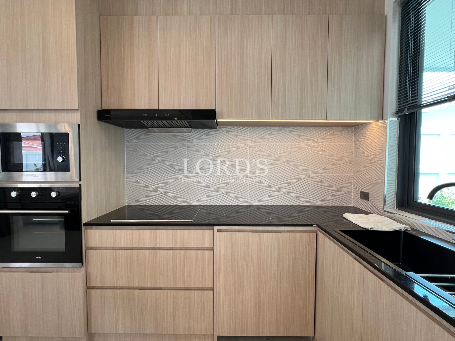 Modern kitchen countertop with built-in cooktop, oven, and textured backsplash.