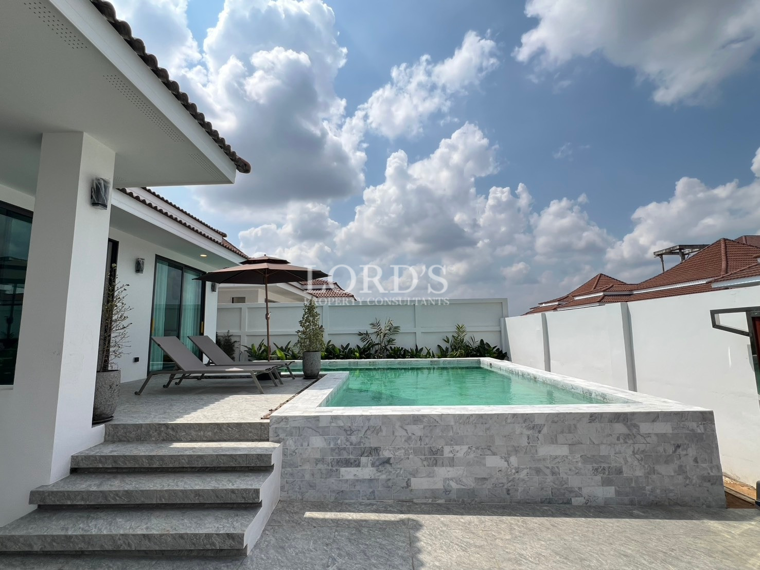 Modern villa swimming pool with raised deck, loungers, and outdoor seating area.