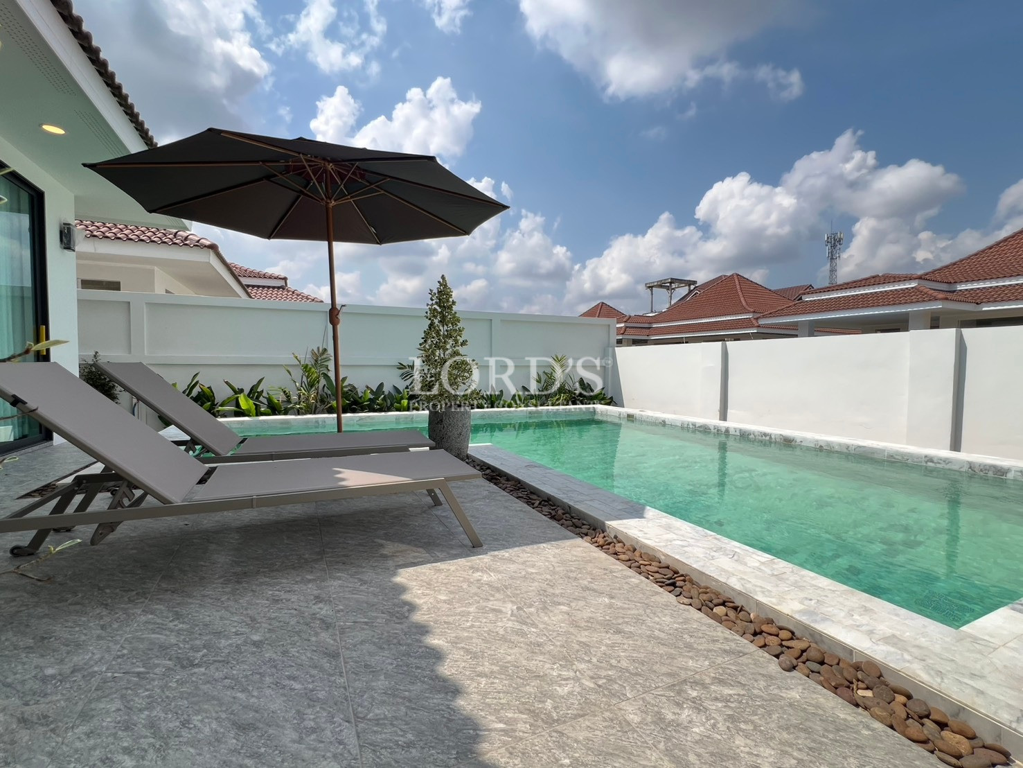 Private swimming pool with sun loungers and umbrella in a modern villa courtyard.