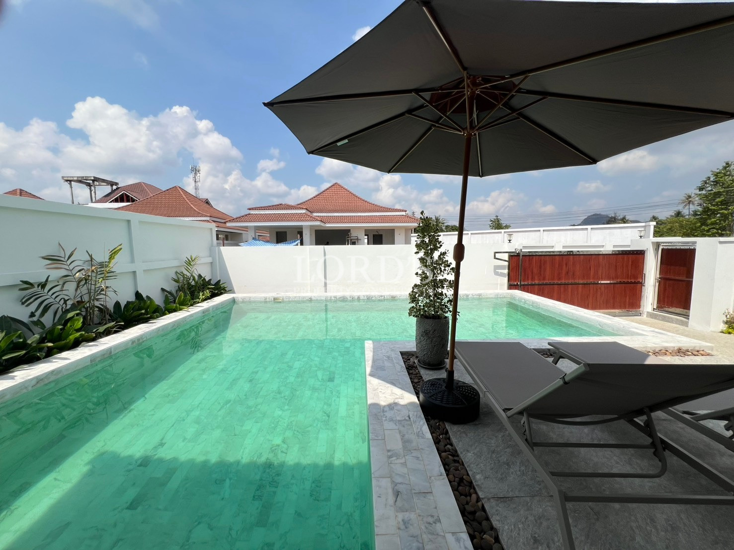 Private swimming pool with sun loungers and large umbrella in a walled courtyard.
