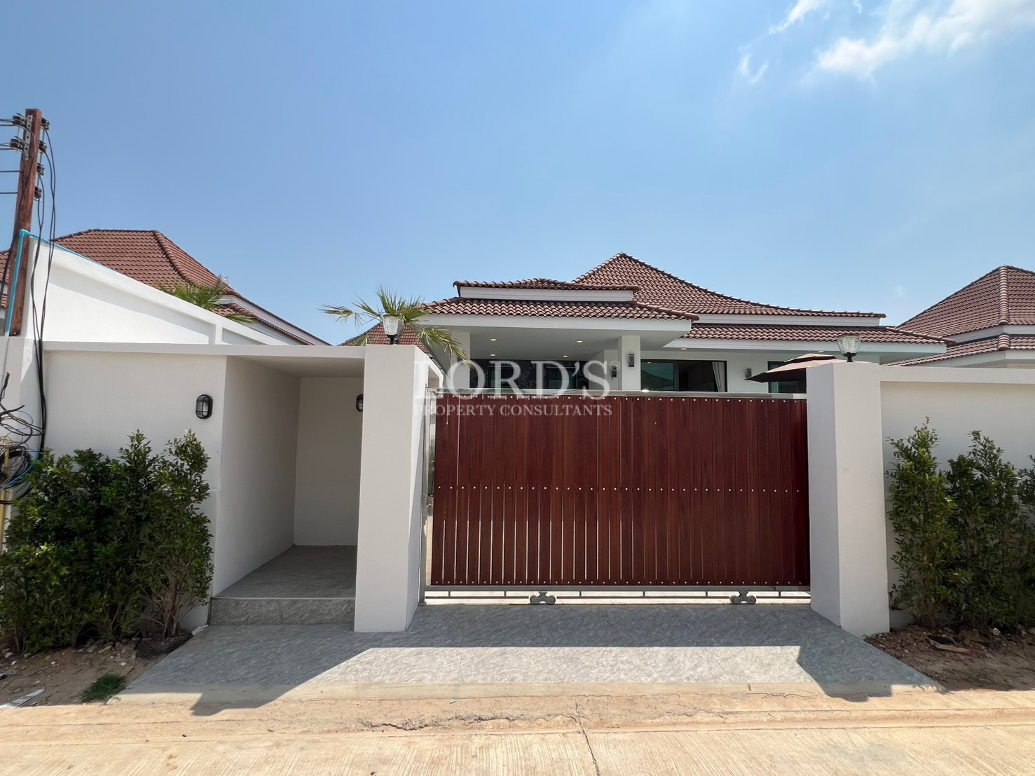 Modern villa exterior with white boundary walls and wooden sliding entrance gate.