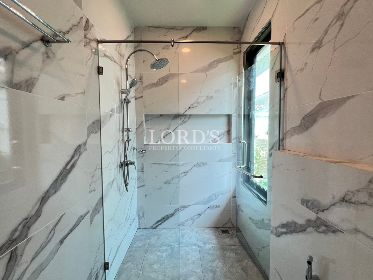 Modern bathroom with marble-look wall tiles, vanity sink, and glass shower enclosure.
