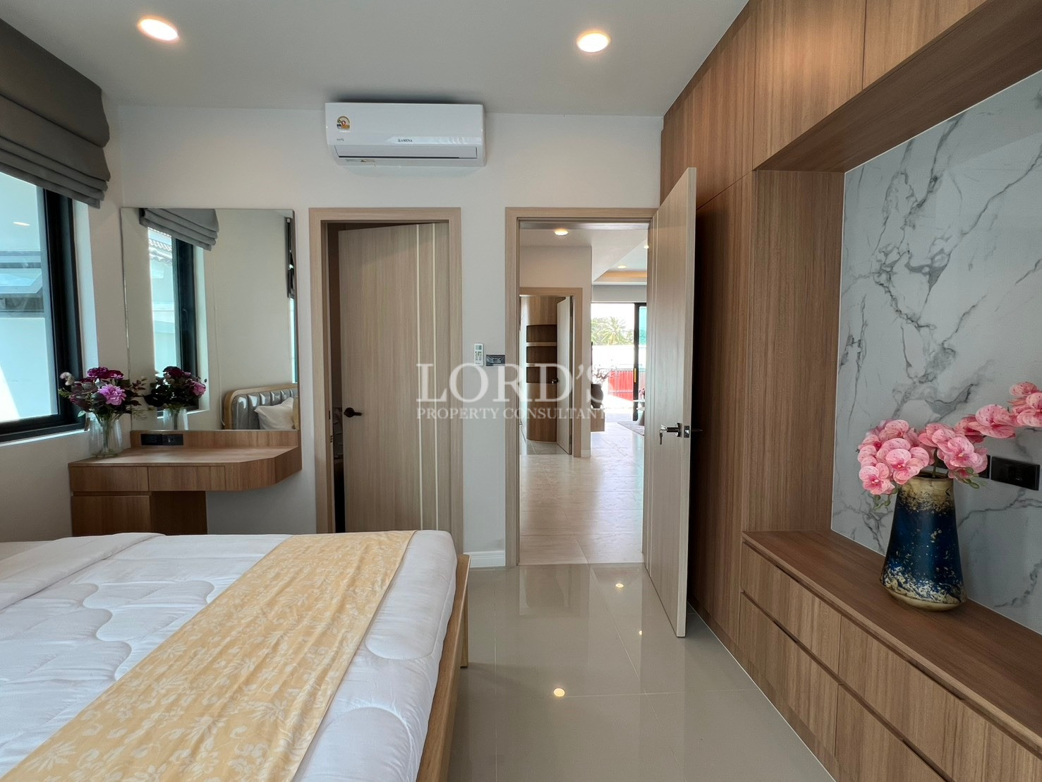 Modern bedroom with built-in wooden wardrobe, vanity desk, and air conditioning.