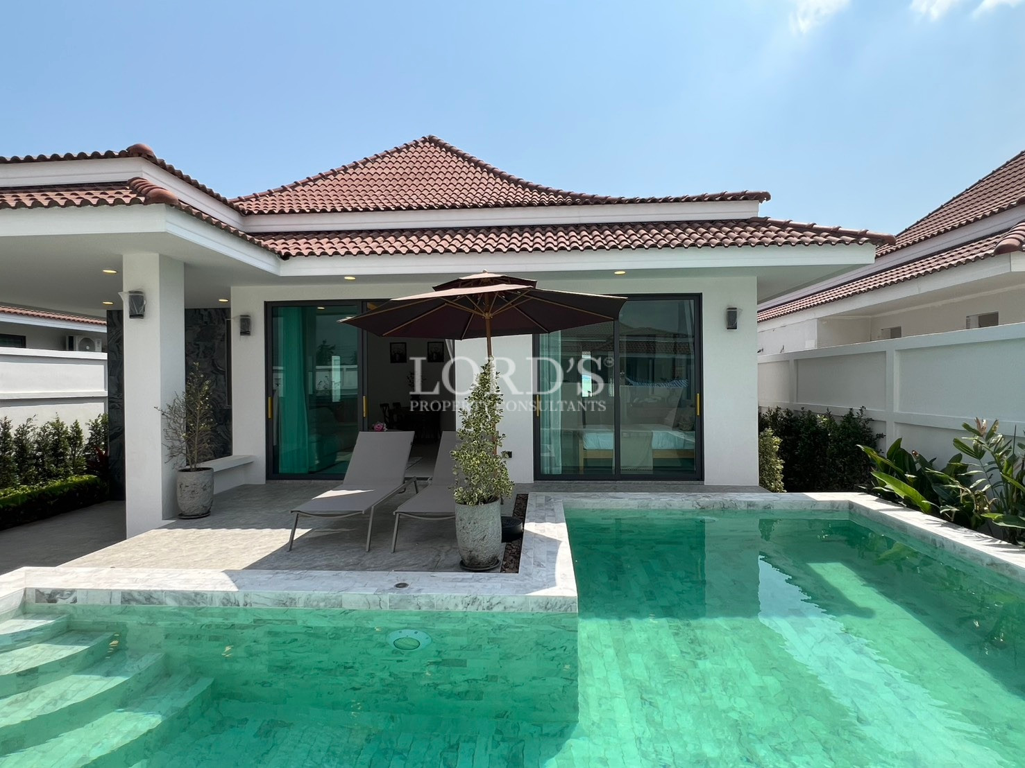 Modern villa with private swimming pool, sun loungers, and shaded patio area.