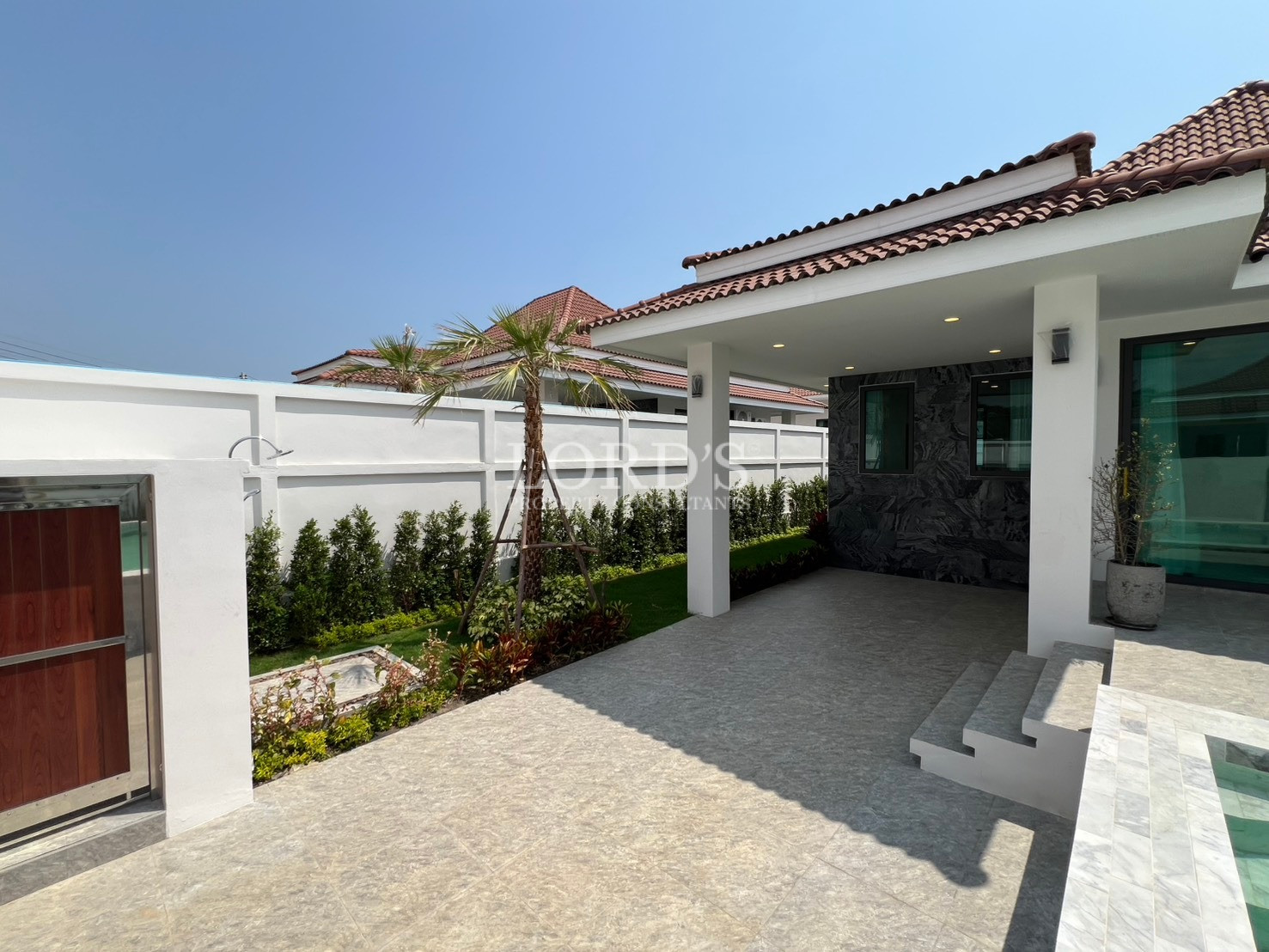 Covered outdoor patio overlooking landscaped garden and outdoor shower area in a modern home.