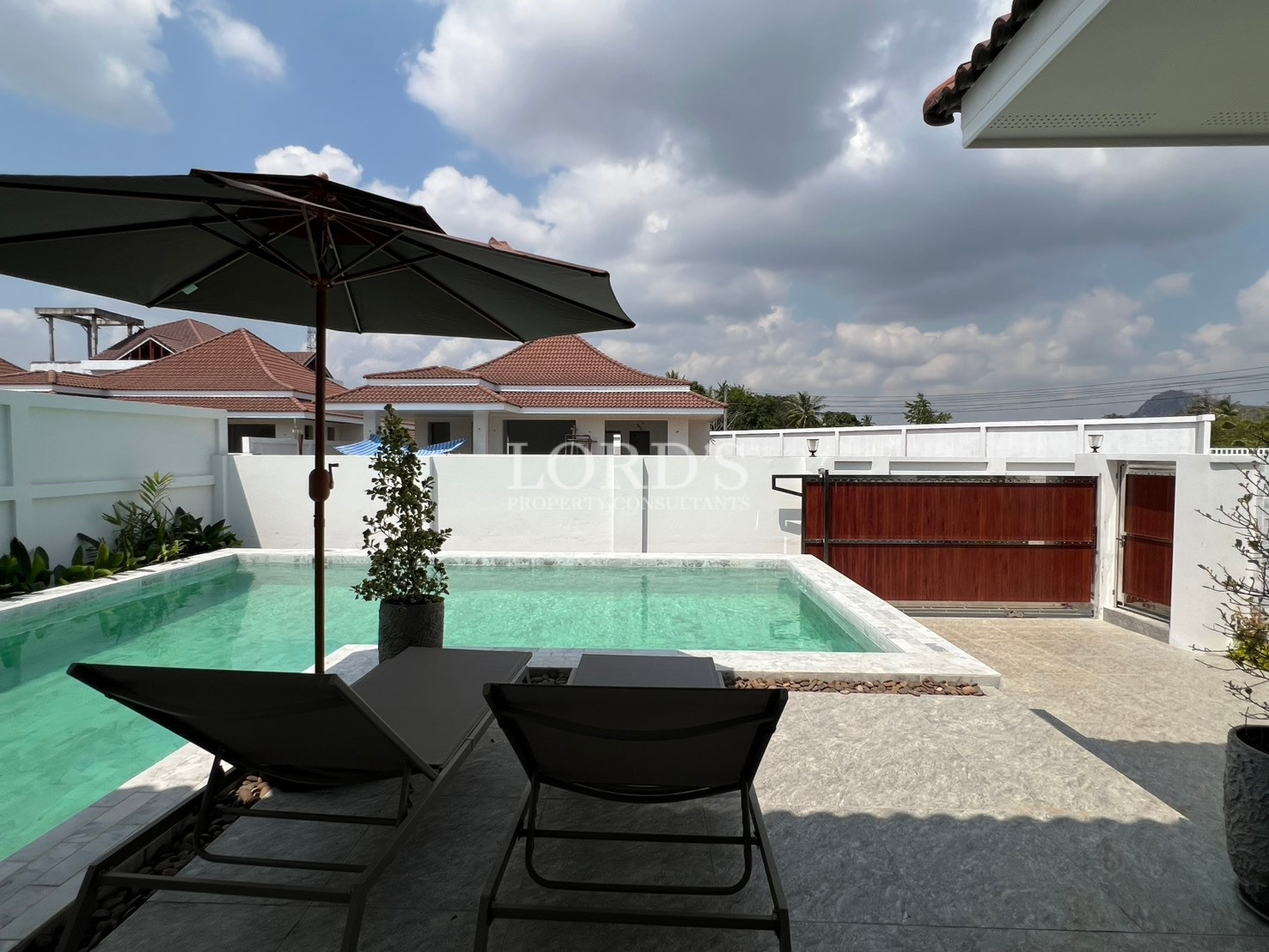 Private swimming pool with sun loungers and umbrella in a modern residential courtyard.