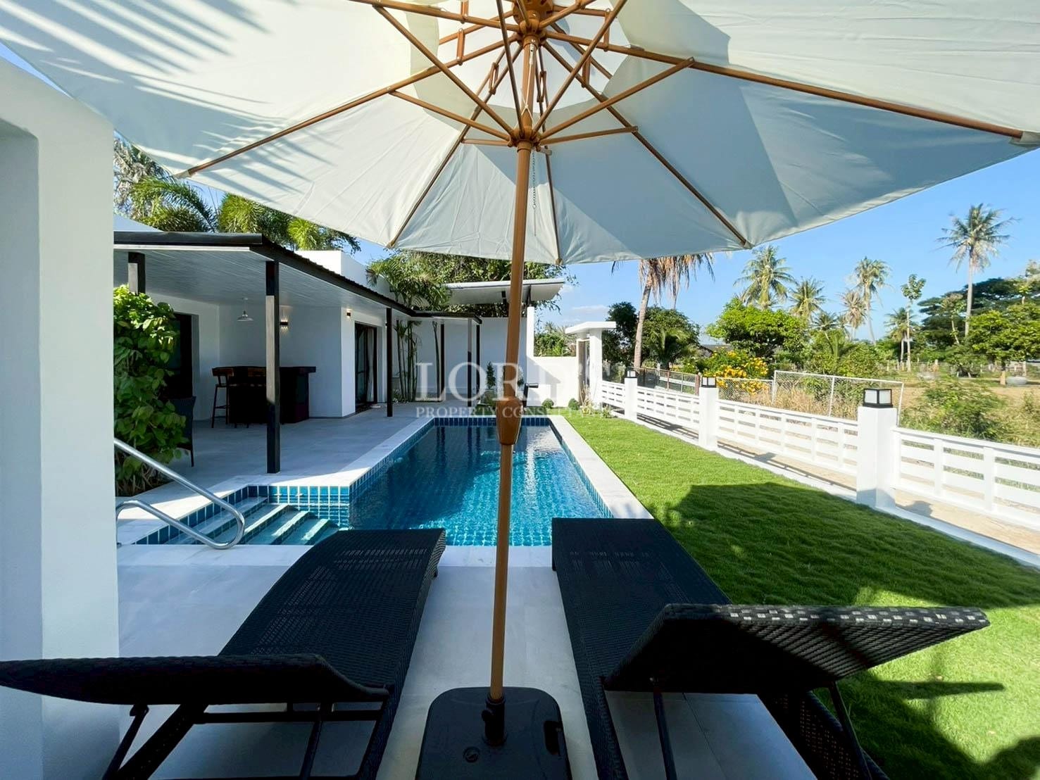 Poolside sun loungers with umbrella beside modern villa