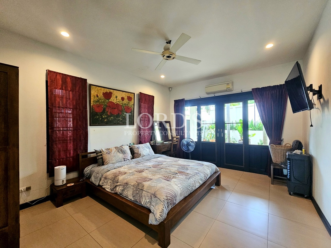 Spacious ensuite bedroom with garden-facing doors, wall-mounted TV, and wooden furnishings