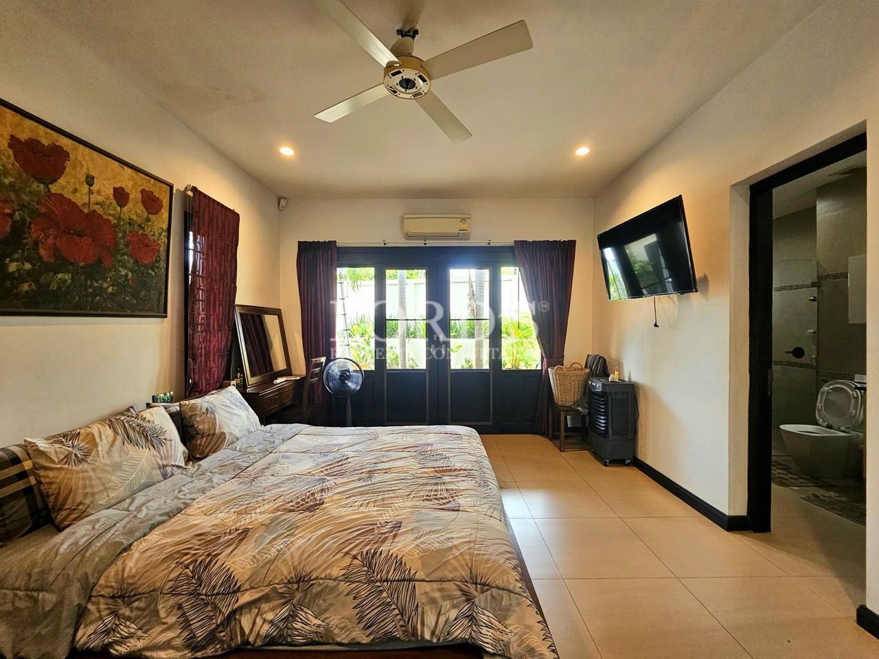 Spacious bedroom with ensuite bathroom, garden-facing doors, and wall-mounted TV