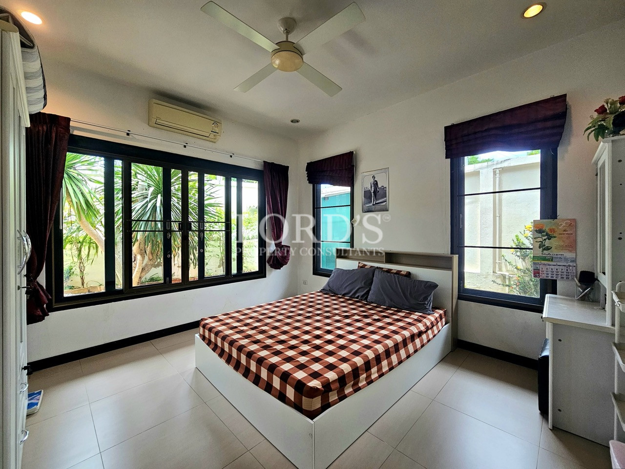Bright guest bedroom with large windows, queen bed, ceiling fan, and garden views