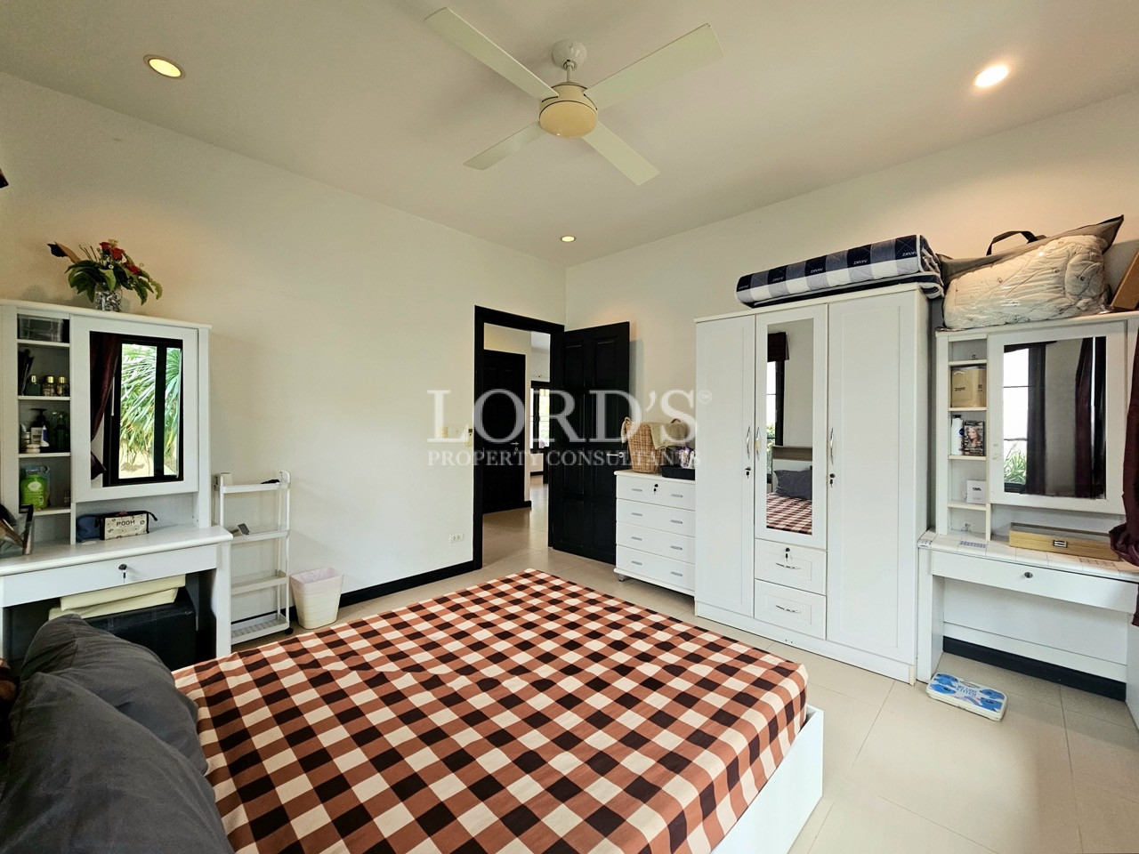 Bright guest bedroom with white furniture, built-in wardrobes, vanity desks, and ceiling fan
