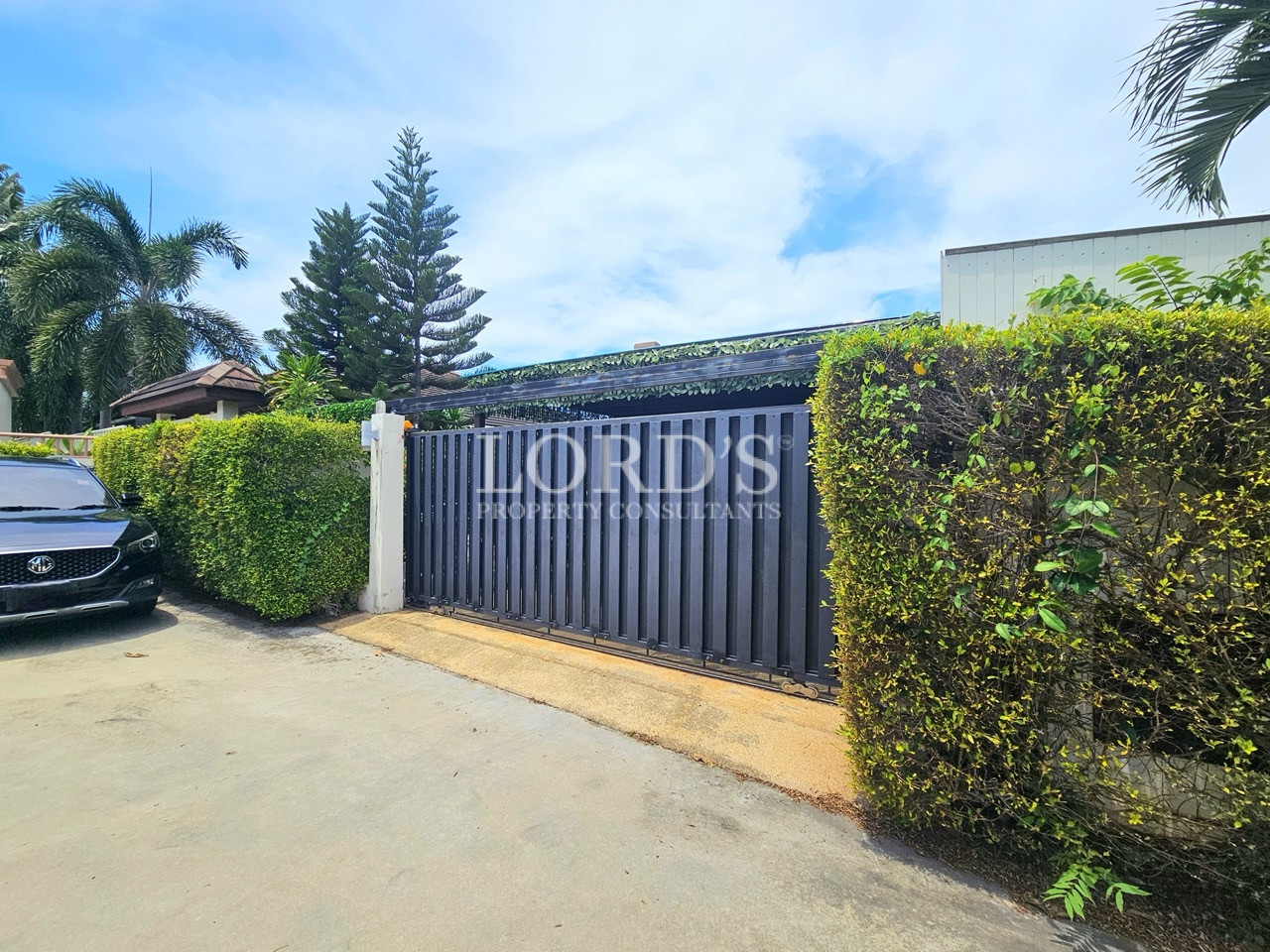 Modern villa entrance with a secure sliding gate, privacy hedges, and landscaped front boundary