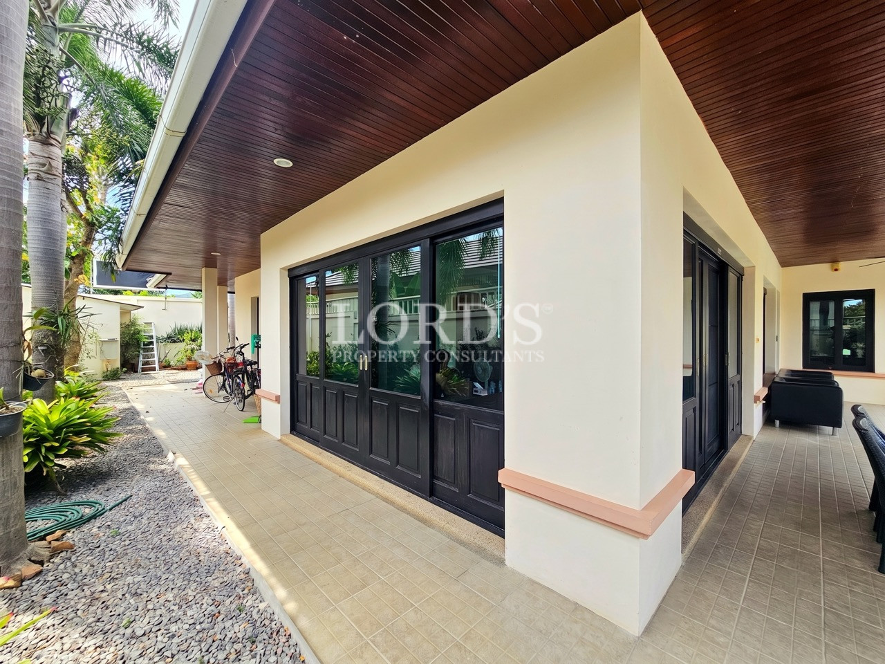 Covered outdoor walkway with black-framed windows, tiled flooring, and landscaped side garden