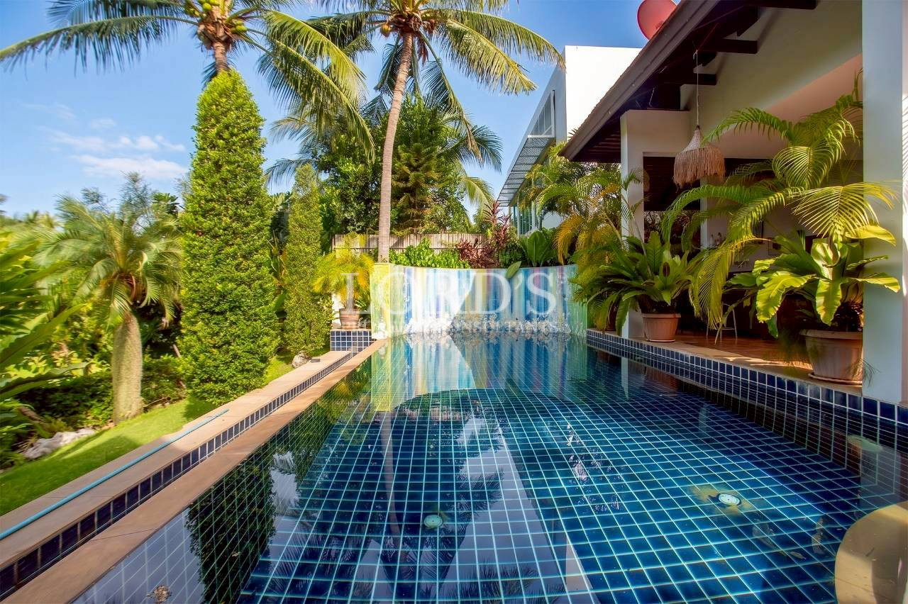 Resort-style swimming pool surrounded by palm trees and luxury villa