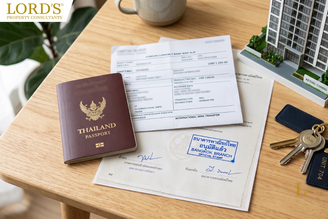 An overhead editorial flat-lay photograph on a warm wooden desk featuring a Thai passport, a foreign currency bank wire slip, and an official Thai bank document stamped in blue. Next to the documents is a set of condo keys on a navy and gold fob, alongside a small architectural model of a condominium building under soft, natural lighting.