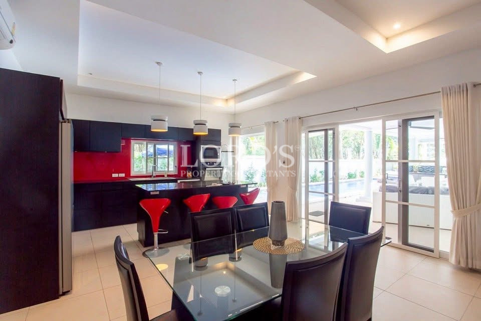 Modern open-plan kitchen and dining area with black cabinetry, red bar stools, glass dining table, and large sliding doors