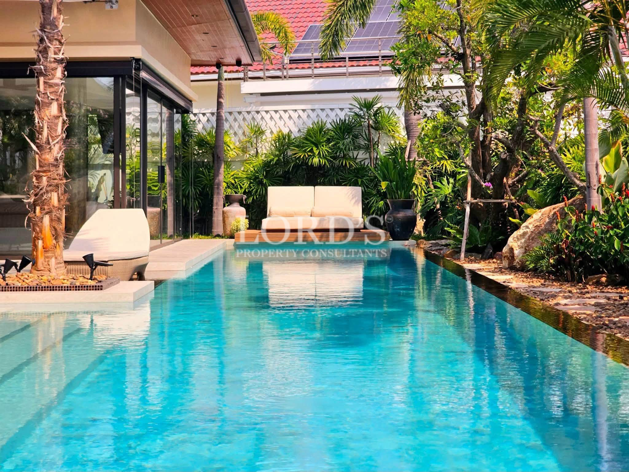 Luxury private swimming pool surrounded by tropical landscaping, sun loungers, and contemporary villa architecture