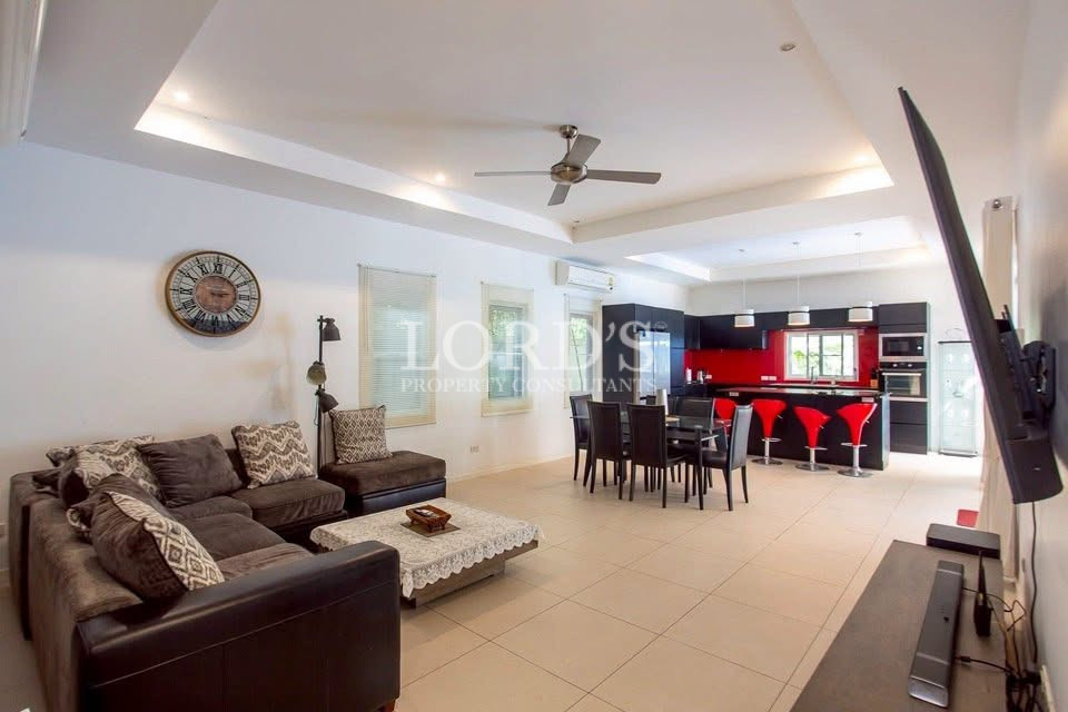 Open-plan living and dining area with a modern kitchen, sectional sofa, dining table, and red bar stools