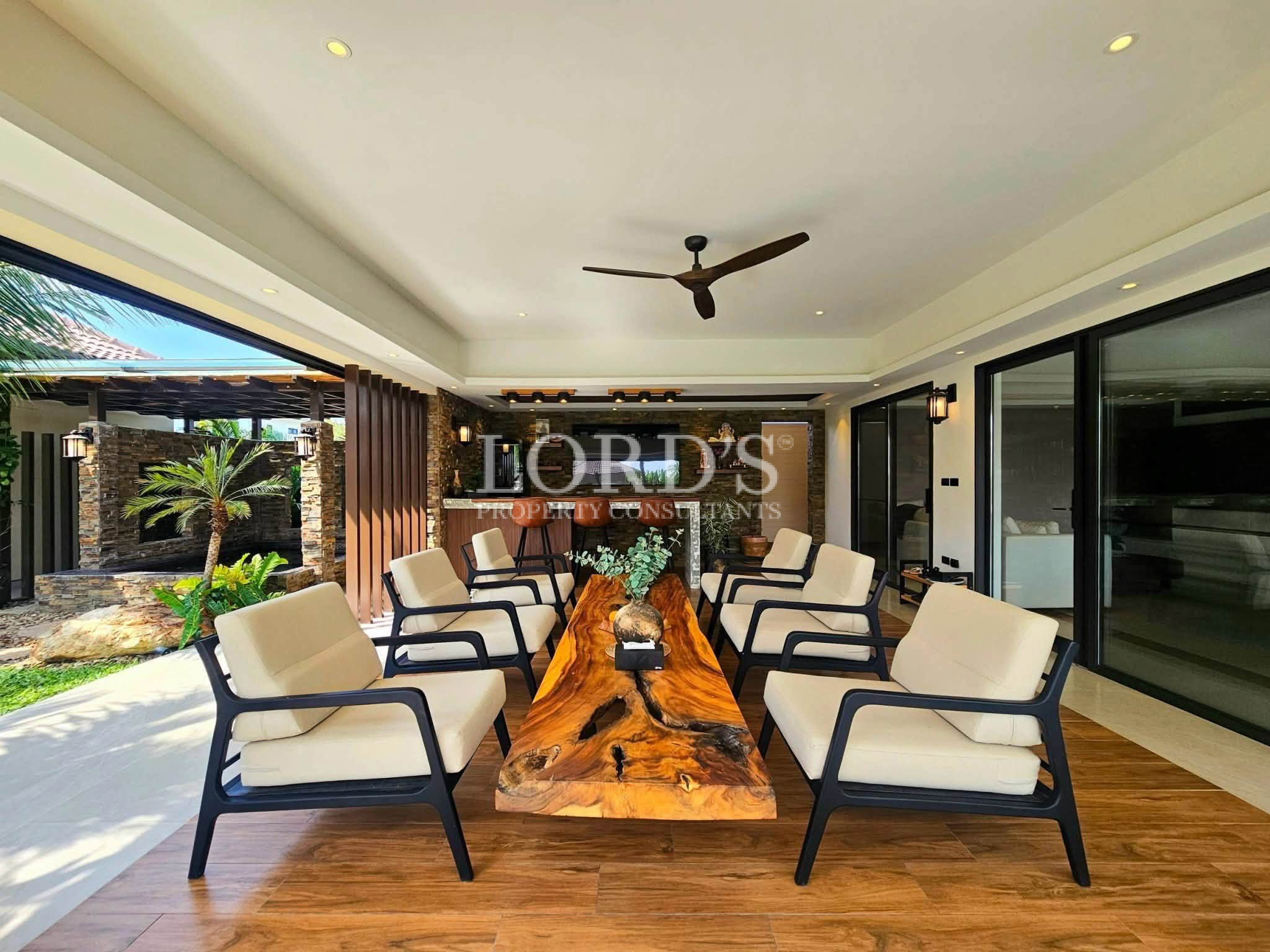 Luxury covered outdoor lounge with modern armchairs, live-edge wooden table, entertainment bar, and tropical courtyard