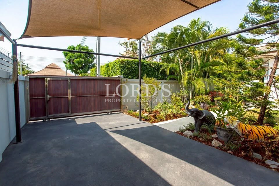 Covered outdoor parking area with a sliding gate, shade canopy, and landscaped tropical garden