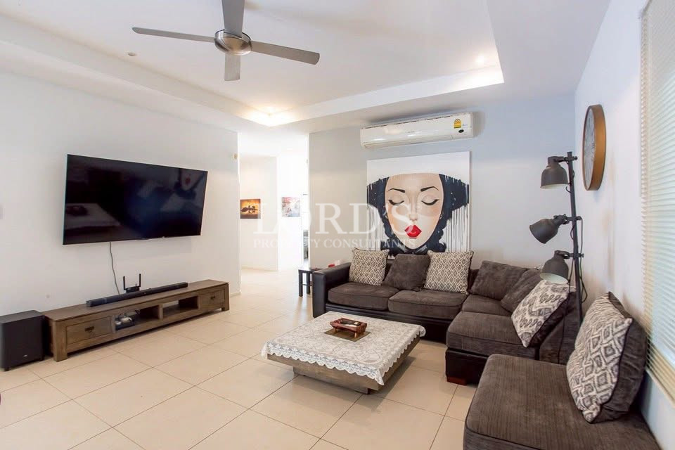 Modern living room with an L-shaped sectional sofa, wall-mounted TV, ceiling fan, air conditioning, and coffee table