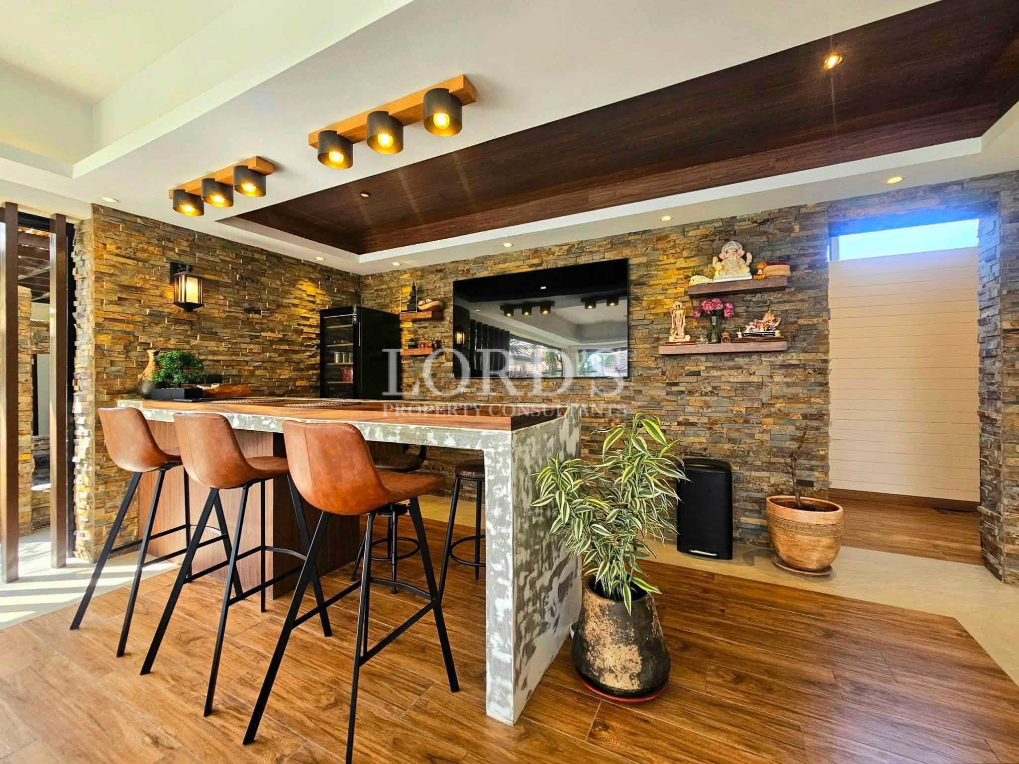 Luxury entertainment bar with marble waterfall island, leather bar stools, natural stone feature walls, and built-in media display