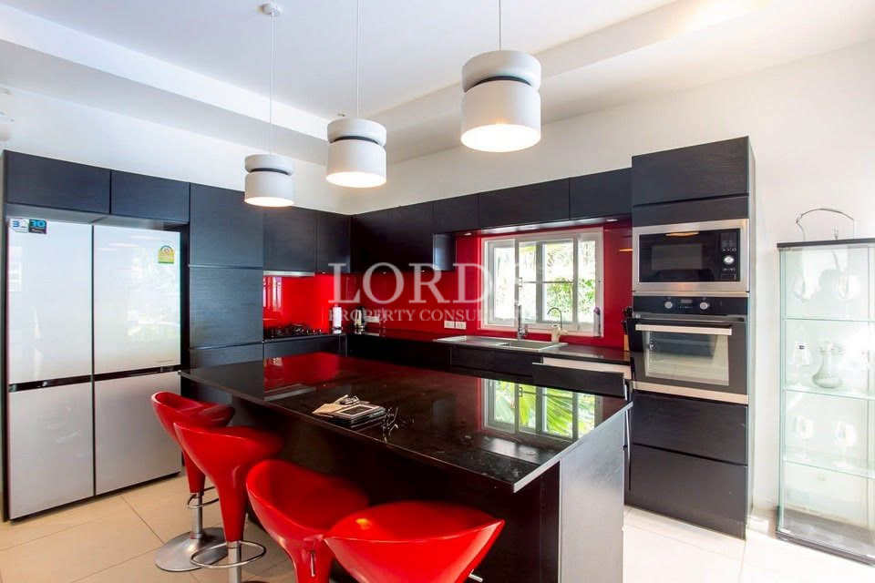 Modern luxury kitchen with a large island, red bar stools, black cabinetry, and built-in appliances