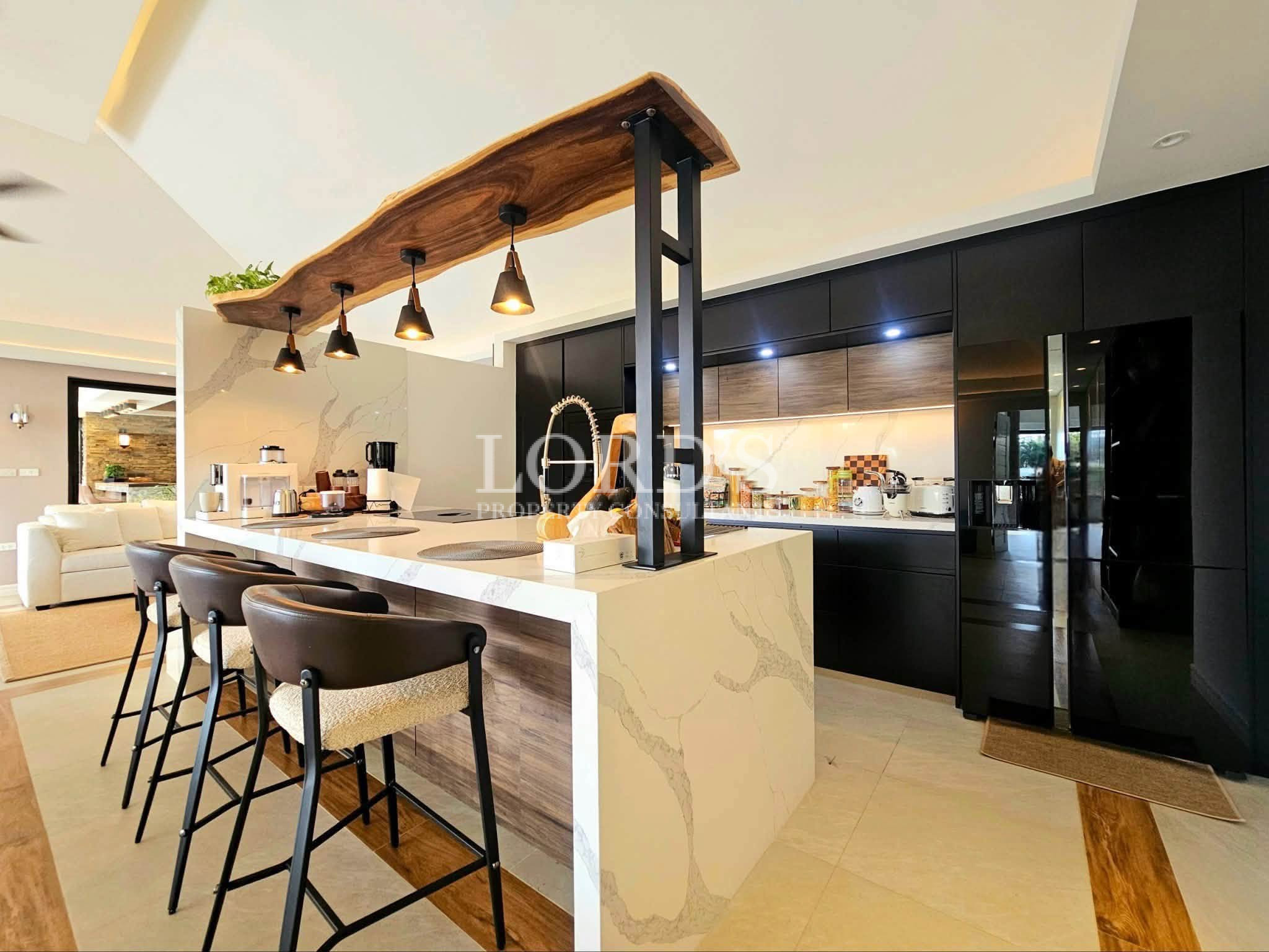 Modern luxury kitchen with waterfall island, breakfast bar, black cabinetry, designer pendant lights, and premium appliances