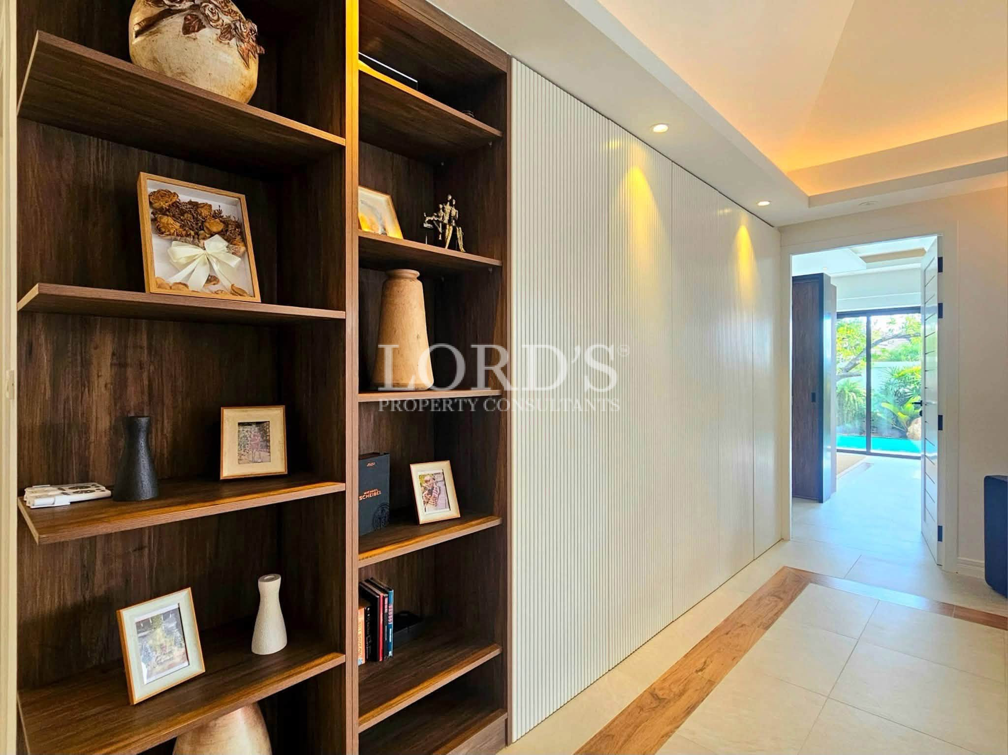 Modern hallway with built-in wooden shelving, decorative display, textured feature wall, and view toward a luxury pool area