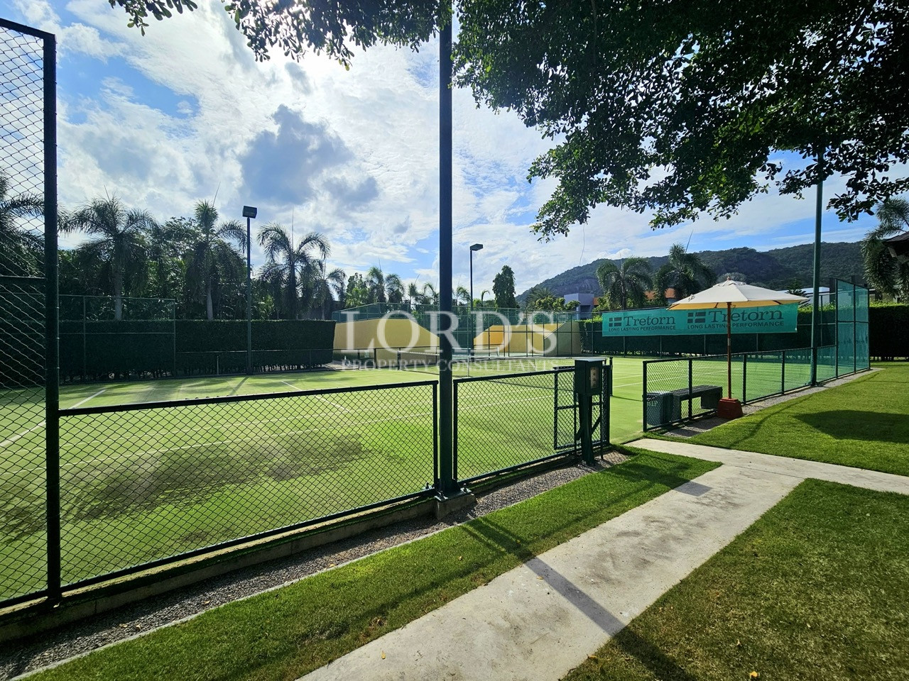 Professional outdoor tennis court with artificial grass surface, perimeter fencing, and landscaped surroundings in a luxury residential community
